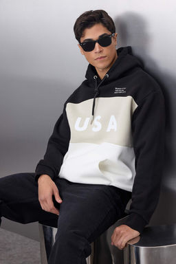TRENDYOL MAN Siyah Oversize/Genis Kesim Renk Bloklu City Bask?l? Kapusonlu Sweatshirt TMNAW25SW00045